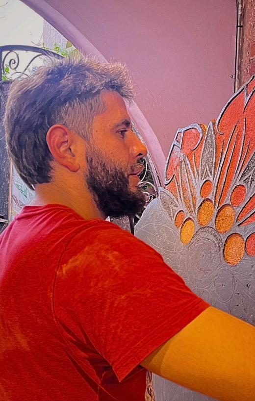 Dan Silva talla con una herramienta un diseño floral en un muro